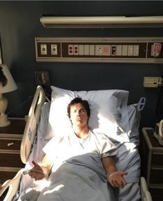 a man laying in a hospital bed with an iv machine on the wall behind him