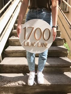 a person standing on some steps holding a sign that says, 700 lila lane in front of them