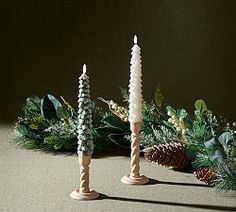 three candles are lined up next to pine cones and greenery