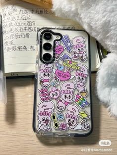 an iphone case with stickers on it sitting next to a teddy bear and pen