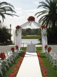 an outdoor ceremony setup with white chairs and red flowers on the aisle, along with palm trees