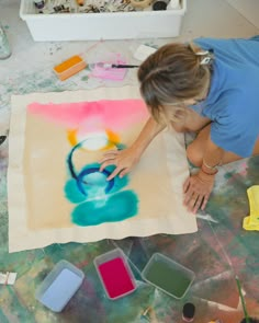 a woman is painting on a large piece of paper with watercolors in front of her