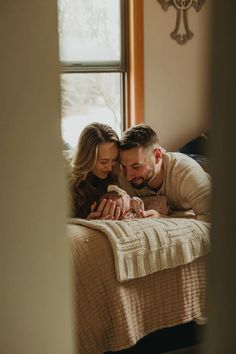 a man and woman laying on top of a bed next to each other holding a baby