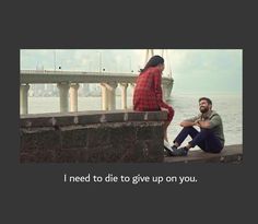 a man and woman sitting next to each other on the edge of a pier with a bridge in the background