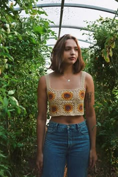 a woman standing in the middle of a garden with sunflowers on her crop top