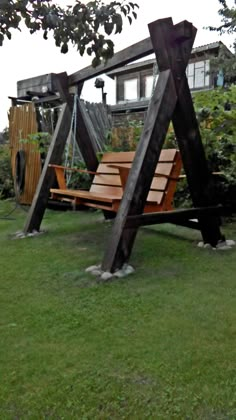 a wooden swing set sitting on top of a lush green field next to a house