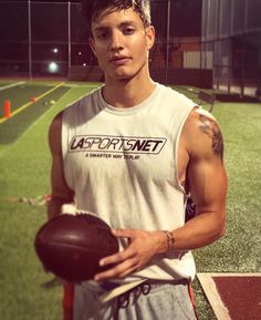 a young man holding a football on top of a field at night with lights in the background