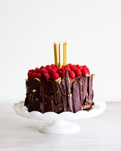 a chocolate cake with raspberries on top and gold candles sticking out of it