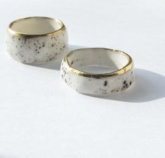 two white and gold rings sitting next to each other on top of a white surface