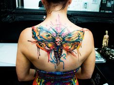 the back of a woman's neck with colorful paint on it and a dragonfly tattoo