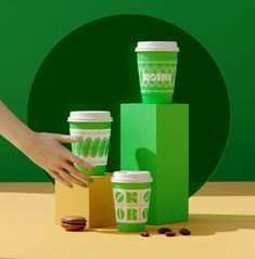 two cups of coffee are being held by a woman's hand next to some boxes