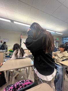 a woman sitting at a desk with her back to the camera, in front of other students