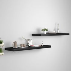 two black floating shelves with plants and books on them in front of a white wall