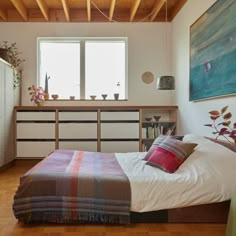 a bed sitting in a bedroom next to a dresser and window with plants on it