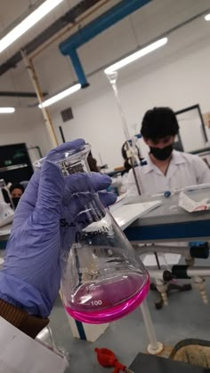 a person in a lab coat and purple gloves holding a flask filled with liquid