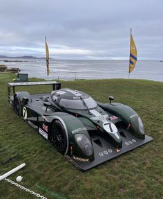 a race car sitting on top of a grass covered field next to the ocean with flags in the background