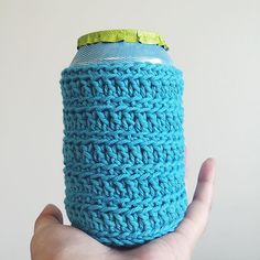 a hand holding a blue crocheted can cooler