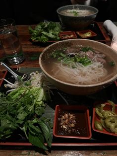 a wooden table topped with bowls filled with soup and veggies on top of it