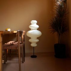 a tall white lamp sitting next to a table with a potted plant on it