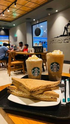 two cups of coffee and some food on a tray in a restaurant with people sitting at tables