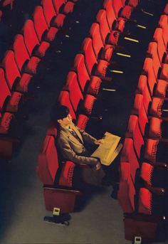 a man is sitting in the middle of rows of red chairs