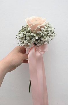 a hand holding a pink rose and baby's breath bouquet with white flowers on it