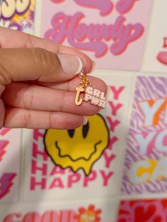 a person is holding a small charm in front of some colorful wallpaper with smiley face stickers