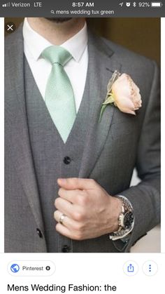 a man in a gray suit with a green tie and flower on his lapel