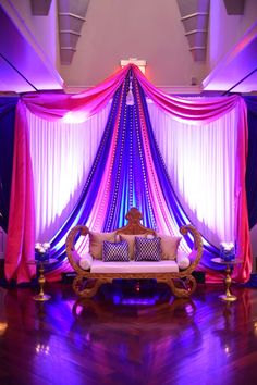 a couch sitting in the middle of a room with purple and pink drapes on it