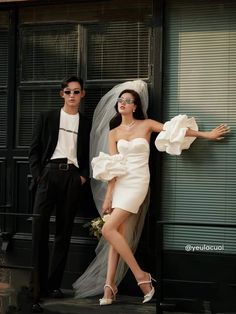 two people standing next to each other in front of a building wearing wedding dresses and veils