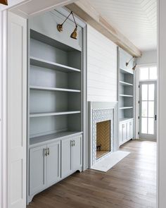 an empty room with built in bookshelves, fireplace and wood floored floors