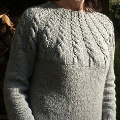 a woman standing in front of a tree wearing a sweater