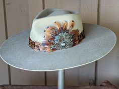 Expertly handcrafted, this wool felt hat is the definition of Nashville fashion. It has a stunning feather hat band and custom made feather fan, that is adorned with a Concho. Perfect for country music and western enthusiasts, this hat is both stylish and unique. The hat is made from 100% wool felt and has a stiff brim that 4" is diameter. The pinch front crown is 4.5" tall. The putty color is a neutral color that will go with just about everything in your wardrobe. Custom Cowgirl Hats, Embellished Cowboy Hat, Feather Hat Band, Art Hats, Nashville Fashion, Cowboy Hat Styles, Hat Burning, Custom Cowboy Hats, Tea Hats