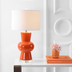 an orange lamp sitting on top of a white table next to a vase with flowers