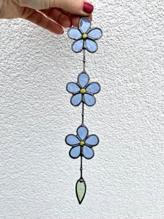 a hand holding up a stained glass flower decoration on a white wall with blue flowers hanging from it's side