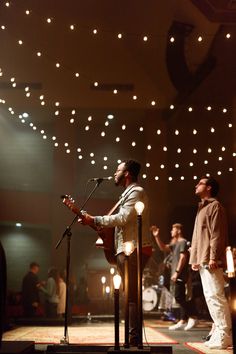 two men are singing into microphones in front of a stage with lights on the ceiling