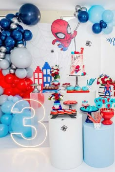 a birthday party with spiderman decorations, balloons and streamers on the wall behind it