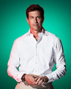 a man in a white shirt and khaki pants poses for a portrait against a green background