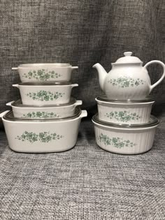 four white dishes with green flowers on them are stacked next to each other and one has a teapot in the middle