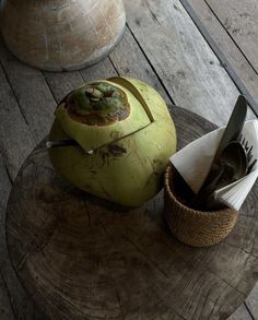 a green apple sitting on top of a wooden table next to a basket filled with utensils