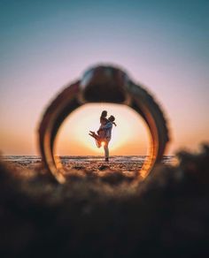 a person standing on top of a sandy beach under a magnifying glass with the sun setting in the background