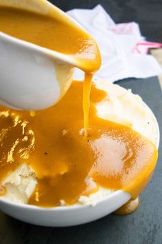 someone pouring gravy over mashed potatoes in a bowl