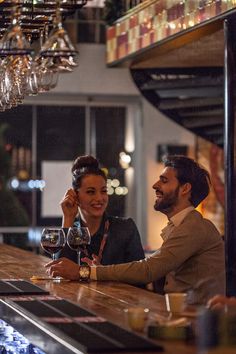 a man and woman sitting at a bar with wine glasses in their hands, smiling