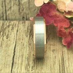 a wedding band with a brushed finish sits on a wooden surface next to some flowers