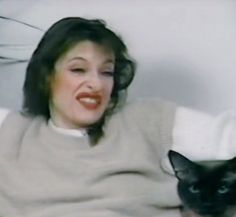 a woman sitting on a couch with a cat in her lap and smiling at the camera