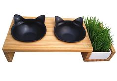 two black cat shaped bowls sitting on top of a wooden table next to green grass