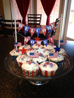 cupcakes are arranged on a cake plate with flags and bunting for the welcome home sign