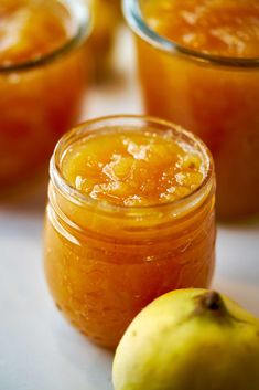 two jars filled with orange marmalade next to an apple