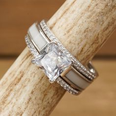 a white gold ring with a princess cut diamond on top and two thin bands around the band