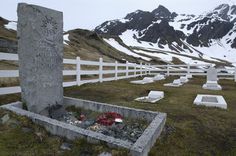 a cemetery in the middle of nowhere with snow covered mountains behind it and flowers growing out of the graves